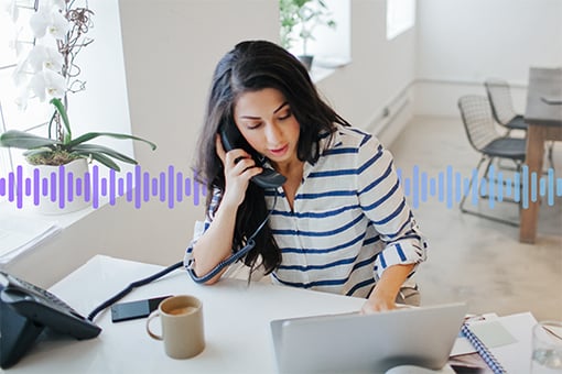 Photo of a woman in an office talking on her desk phone while typing on her computer. In the background, a series of small vertical purple-gradient lines run across the screen.