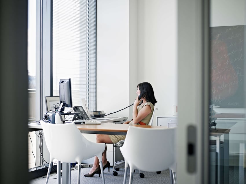 Businesswoman sitting at desk in office talking on phone smiling