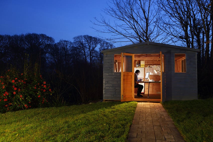 Individual working inside a small outdoor shack which is lit up as night starts to fall