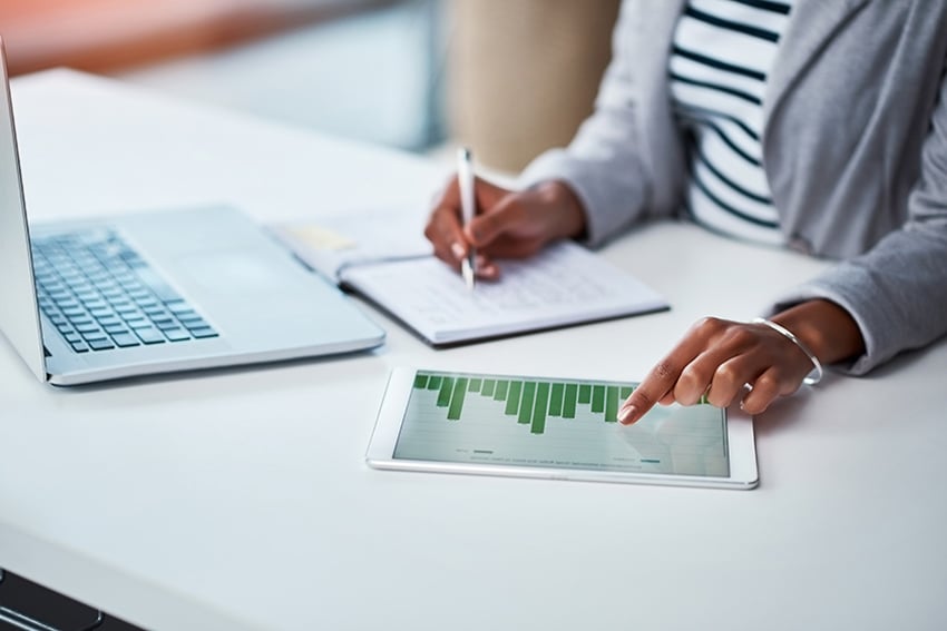 1041512864 Person writing down financial info from chart and laptop in front of her