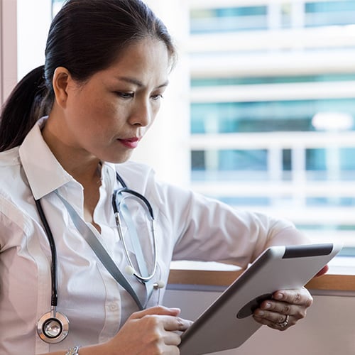 Female Asian doctor looking at a smart device while on her shift